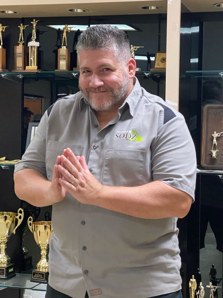 Bill Koeppen poses in front of a trophy case